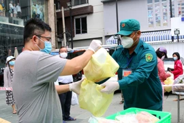 Lực lượng chức năng phường 12, quận 3 hỗ trợ người dân mua hàng hóa, thực phẩm các loại và trứng tại điểm xe bán hàng lưu động của Sở Công thương thành phố. (Ảnh: Thanh Vũ/TTXVN)