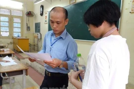 Cán bộ coi thi đối chiếu thông tin thí sinh. (Ảnh: Phạm Mai/Vietnam+)