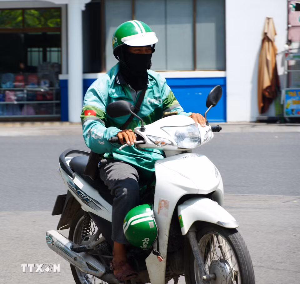 Lái xe công nghệ mặc đồ bảo hộ chống nắng nóng gay gắt khi di chuyển trên đường Trần Hưng Đạo, phường Phú Xuân, thành phố Huế. (Ảnh: Nguyên Lý/TTXVN)