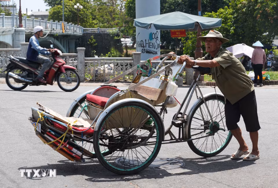 Nhọc nhằn đẩy xe xích lô lên dốc giữa nắng nóng gay gắt ở gần cầu Gia Hội, phường Phú Xuân, thành phố Huế. (Ảnh: Nguyên Lý/TTXVN)