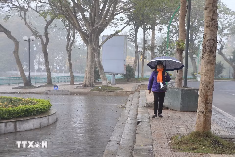 Người dân phải dùng ô vì trời xuất hiện mưa phùn, mưa nhỏ ở khu vực đường Thanh Niên và Hồ Tây. (Ảnh: Nguyễn Hoa/TTXVN phát)