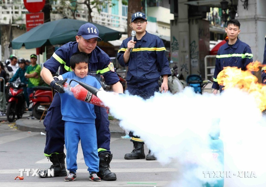 Chiến sỹ cảnh sát phòng cháy chữa cháy hướng dẫn trẻ em xử lý đám cháy nhỏ ngay tại không gian phố đi bộ hồ Hoàn Kiếm (Hà Nội, 2023). (Ảnh: Phạm Kiên/TTXVN)