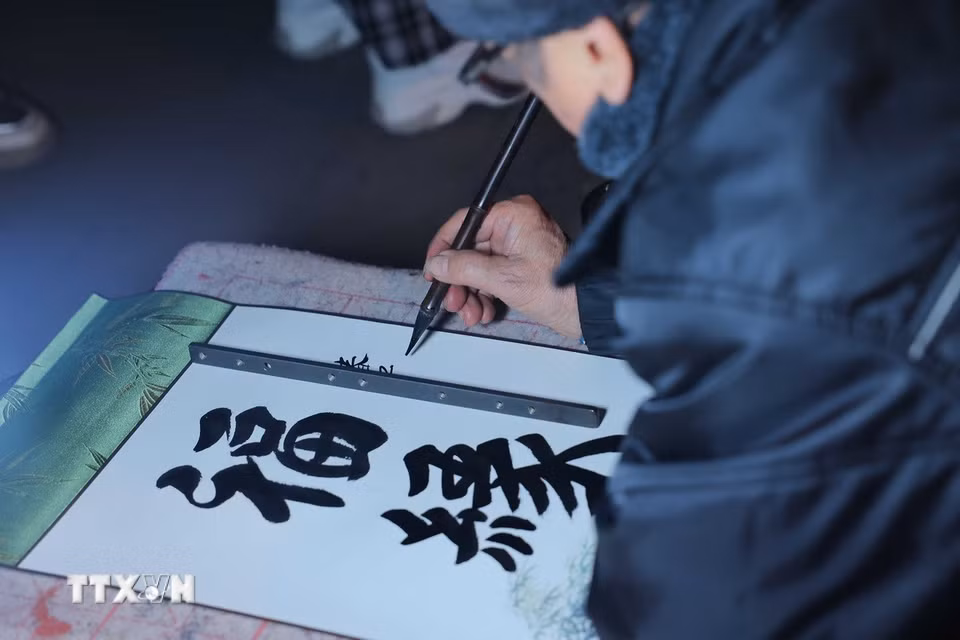 Những ông đồ, bà đồ (thường là những người cao tuổi có tài viết chữ đẹp) sẽ viết chữ cho khách với những nét chữ thư pháp thanh thoát, uyển chuyển. (Ảnh: Hoàng Hiếu/TTXVN)