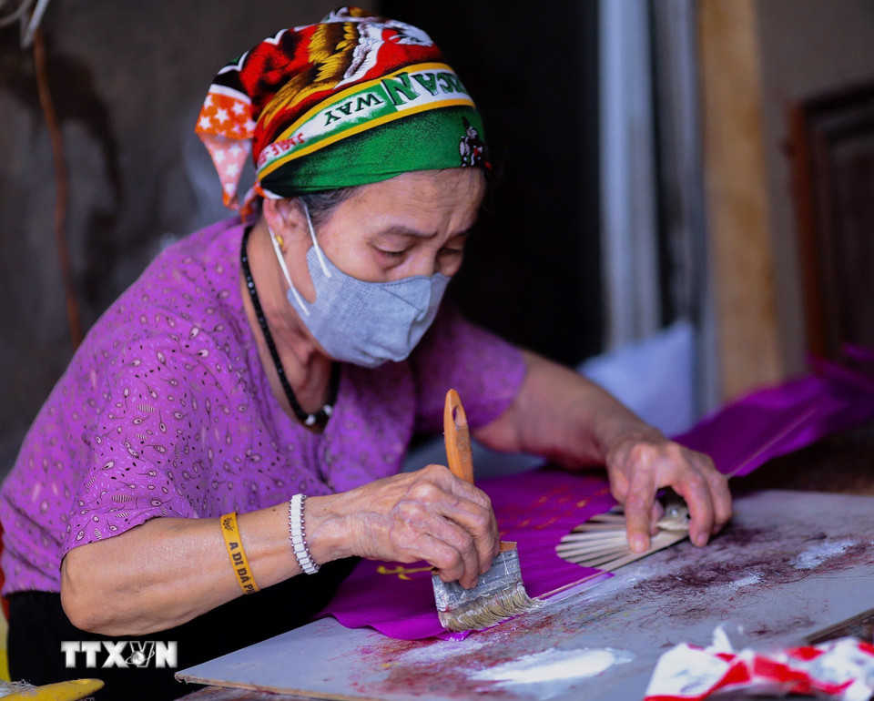 Đôi tay người thợ già cẩn trọng vuốt keo cho từng lớp giấy, lưu giữ tinh thần thủ công qua từng chiếc quạt. (Ảnh: Phương Anh/TTXVN phát)