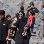 Người dân Palestine đứng trên đống đổ nát sau các cuộc không kích của Israel xuống Dải Gaza. (Ảnh: IRNA/TTXVN)