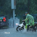 Nhiều người đi xe máy phải xuống dắt bộ vì mưa quá lớn. (Ảnh: Hoàng Hiếu/TTXVN)