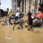 Một em nhỏ cùng những người lớn trong dòng nước lũ ở Sylhet, Bangladesh, ngày 19/5/2022. (Ảnh: AFP/TTXVN)