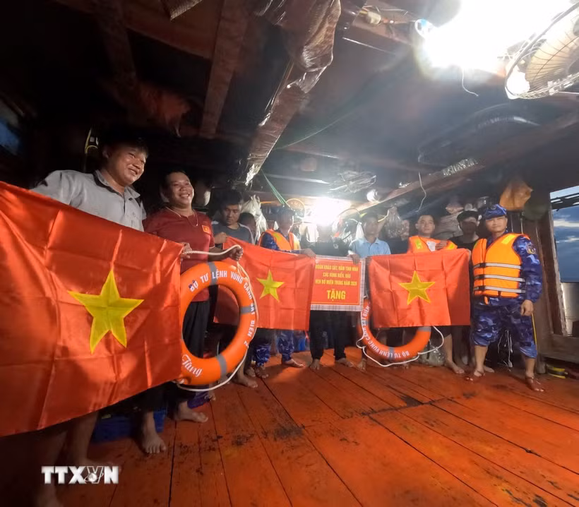 Cán bộ, chiến sỹ Bộ Tư lệnh Vùng Cảnh sát biển 2 trao cờ Tổ quốc và quà động viên ngư dân yên tâm vươn khơi, bám biển, chấp hành đúng các quy định trong khai thác thủy sản. (Ảnh: Xuân Quý/TTXVN)