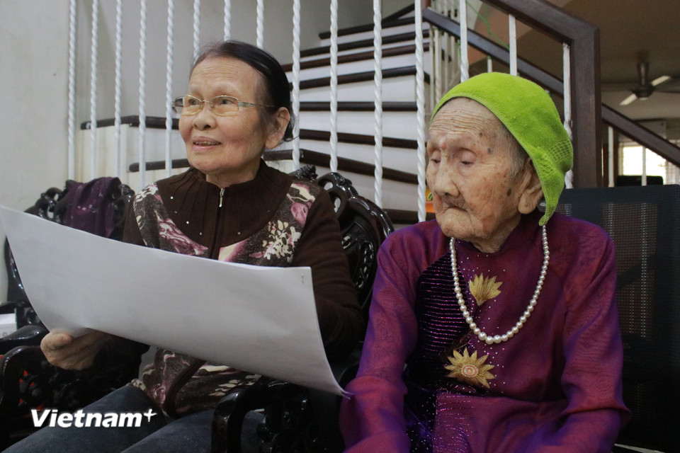 Ở tuổi 99, Mẹ Nguyễn Thị Tẹo luôn có con gái - bà Chiên - ở bên săn sóc. Bà Chiên kể mỗi khi đón các đại diện cơ quan đoàn thể, tổ chức chính trị đến thăm hỏi và tri ân, Mẹ lại xúc động nhớ về chồng con và ngày tháng cơ hàn cùng đất nước trải qua gian khó. (Ảnh: Minh Anh/Vietnam+)
