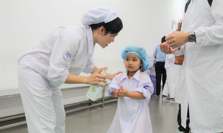 Trước khi vào tham quan, các bạn nhỏ được các cô chú nhân viên tại nhà máy hướng dẫn về cách di chuyển trong nhà máy, mặc trang phục bảo hộ và rửa tay đúng theo quy định của nhà máy. ( Ảnh: PV)