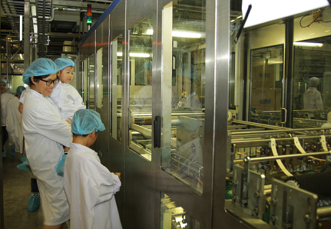 Bé thích thú khi được mẹ giới thiệu về dây chuyền đóng gói sữa. (Ảnh: PV)