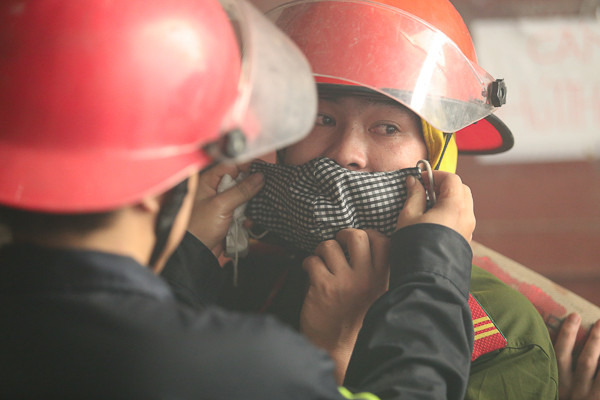 Một chiến sĩ cứu hỏa đeo khẩu trang cho đồng đội để tránh khói bụi. (Ảnh: Minh Chiến/Vietnam+) 