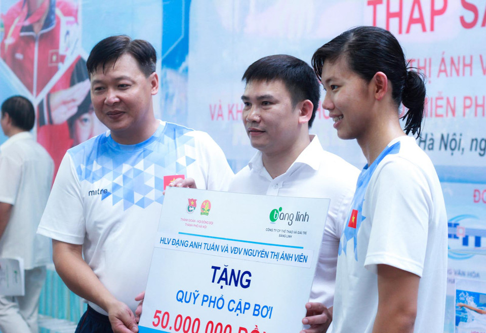 Ở chiều ngược lại, huấn luyện viên Đặng Anh Tuấn (ngoài cùng trái) và Ánh Viên (ngoài cùng phải) ủng hộ quỹ phổ cập bơi cho trẻ em có hoàn cảnh khó khăn. (Ảnh: Hiếu Lương/Vietnam+)