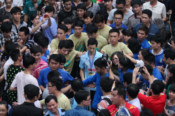 Tiến Minh chỉ có thể rời sân trong sự bảo vệ của các tình nguyện viên (áo xanh và áo vàng). (Ảnh: Minh Chiến/Vietnam+) Việc Tiến Minh đăng quang một cách dễ dàng trong trận chung kết Ciputra Hà Nội hôm qua (30/3) đã “kích nổ” bầu không khí hâm mộ cuồng nhiệt của người hâm mộ thủ đô. Nhà thi đấu Cầu Giấy đã có một tuần (25-30/3) rực lửa trong thời gian giải Ciputra Hà Nội - Yonex Sunrise 2014 diễn ra. Tâm điểm của giải đấu đương nhiên nằm ở cái tên Nguyễn Tiến Minh - hạt giống số một, vận động viên hiếm hoi của Việt Nam đạt đẳng cấp thế giới. Chiến thắng của Tiến Minh trong trận chung kết hôm qua đã khiến bầu không khí cuồng nhiệt đạt tới đỉnh điểm. Ban tổ chức đã tỏ ra khôn ngoan khi xếp trận chung kết đơn nam của Tiến Minh (lúc 16 giờ) là cuộc đấu cuối cùng. Dù vậy, ngay từ khoảng 14 giờ, nhà thi đấu Cầu Giấy đã gần như kín chỗ. Đến 15 giờ, khán giả đã không thể chen vào nhà thi đấu. Rất nhiều cổ động viên đã phải ngồi bệt, ngồi trên cầu thang, thậm chí trèo lên cả cửa sổ.