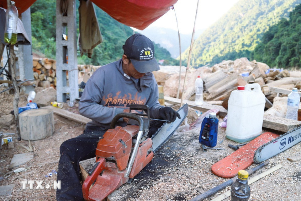 Người dân sử dụng cưa xăng để xẻ và sơ chế gỗ tại các điểm tập kết bên bờ sông Nậm Nơn. (Ảnh: Xuân Tiến/TTXVN)