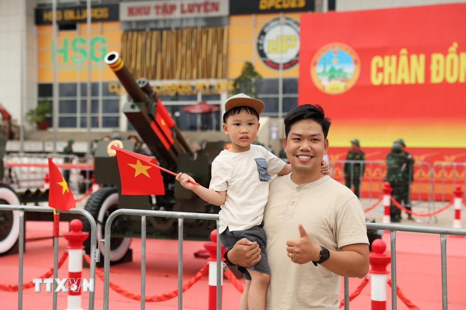 Một em bé hào hứng cầm lá cờ Tổ quốc trong vòng tay cha để lưu lại những hình ảnh cùng dàn pháo lễ tại Sân vận động Mỹ Đình. (Ảnh: Vũ Quang/TTXVN)