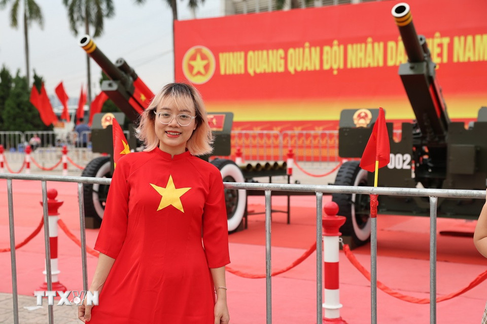 Một bạn trẻ mặc áo dài truyền thống với họa tiết lá cờ Tổ quốc, tươi cười rạng rỡ bên cạnh dàn pháo. (Ảnh: Vũ Quang/TTXVN)
