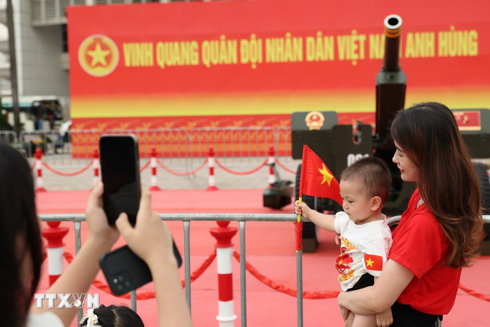Các em nhỏ được bố mẹ cho mang cờ Tổ quốc để chụp ảnh cùng dàn pháo lễ. (Ảnh: Vũ Quang/TTXVN)
