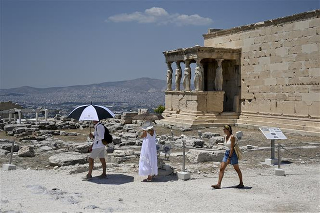 Khách du lịch di chuyển dưới thời tiết nắng nóng tại Athens, Hy Lạp. (Ảnh: AFP/TTXVN) Chuyên gia Thụy Điển cảnh báo về các đợt nắng nóng tại châu Âu ảnh 1