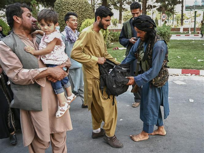 Một tay súng Taliban kiểm tra hành lý của người dân tại khu vực sân bay Kabul, Afghanistan. (Ảnh: AFP/TTXVN|) Tình hình Afghanistan: HCNR kêu gọi Taliban đảm bảo công bằng xã hội ảnh 1