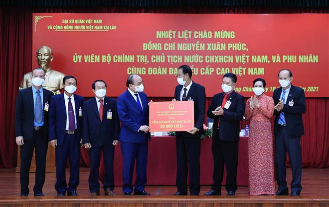 Chủ tịch nước Nguyễn Xuân Phúc trao số tiền ủng hộ cộng đồng người Việt Nam tại Lào khắc phục khó khăn do dịch COVID-19 gây ra. (Ảnh: Thống Nhất/TTXVN) Chủ tịch nước gặp đại diện cộng đồng và doanh nghiệp Việt Nam tại Lào ảnh 3