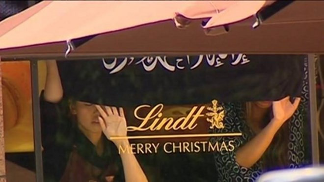 Các con tin đứng bên trong quán Lindt Chocolat Cafe với 2 tay đặt lên cửa sổ, dưới lá cờ đen có chữ Arab. Australia: Có khoảng 30 con tin trong vụ bắt cóc ở Sydney ảnh 1