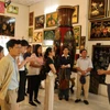 Khách tham quan lắng nghe giới thiệu về lịch sử tranh sơn mài tại cơ sở sản xuất sơn mài Định Hoà. (Ảnh: Khánh Ly/Vietnam+)