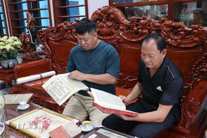 Die Kunsthandwerker Nguyen Cong Trang (rechts) und Nguyen Cong Dat besprechen Dokumente und Artefakte im Zusammenhang mit dem Holzschnitt- und Druckgewerbe. (Foto: Manh Minh/VNA) ttxvn-hai-phong-bao-ton-nghe-khac-in-moc-ban-4.jpg