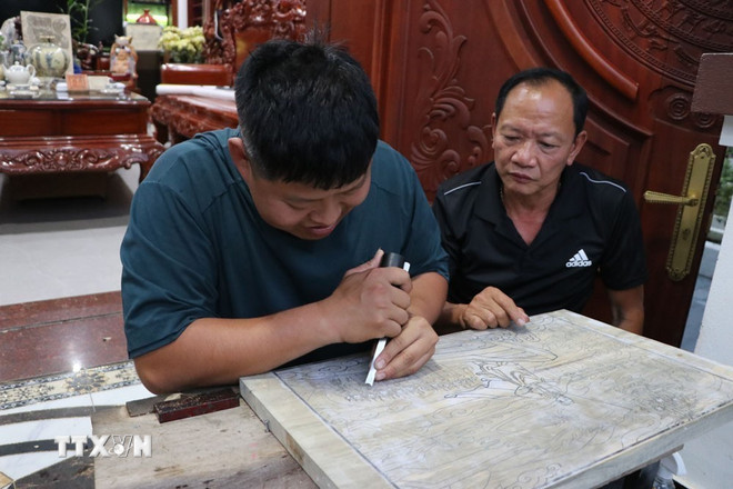 Der Kunsthandwerker Nguyen Cong Trang (rechts) berät Nguyen Cong Dat beim Gravieren und Drucken von Holzschnitten. (Foto: Manh Minh/VNA) ttxvn-hai-phong-bao-ton-nghe-khac-in-moc-ban-3.jpg