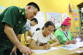 Thiếu tá Lò Thanh Chuyển, Đồn Biên phòng Leng Su Sìn, đến lớp học xóa mù chữ tại bản Cà Nà Pá để hỗ trợ giáo viên và các học viên tại đây. (Ảnh: Trung Kiên/TTXVN)