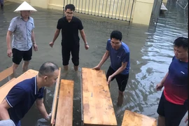 Các thầy cô giáo Trường Tiểu học Nam Trung Yên đã kê bàn ghế làm cầu giúp phụ huynh đón con, học sinh không bị dầm nước. (Ảnh: PHCC)