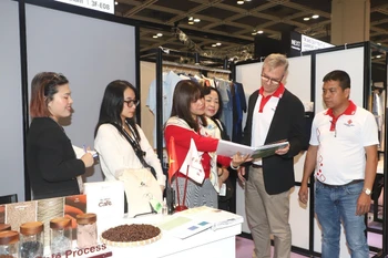 Khách hàng tìm hiểu thông tin về các sản phẩm thời trang làm từ bã càphê và sợi dứa của doanh nghiệp Việt Nam. (Ảnh: Xuân Vịnh/TTXVN)