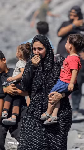 Người dân Palestine đứng trên đống đổ nát sau các cuộc không kích của Israel xuống Dải Gaza. (Ảnh: IRNA/TTXVN)
