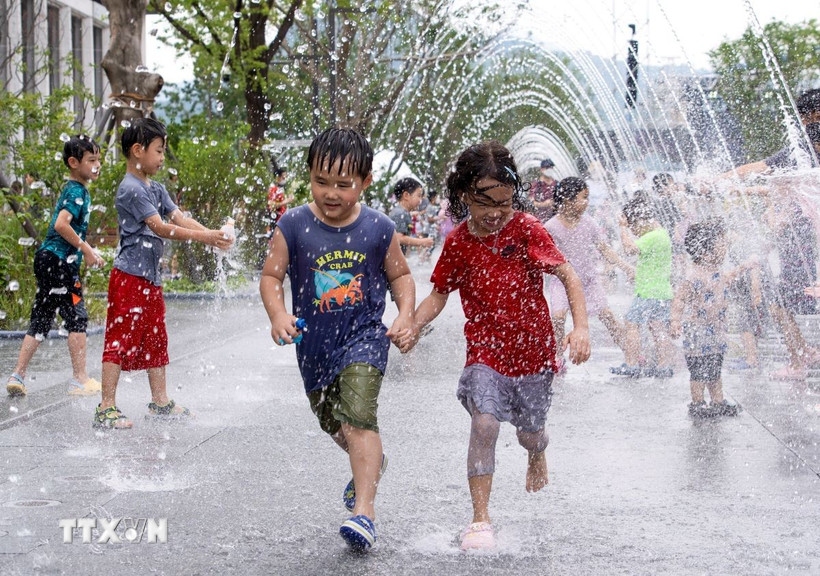 Các em nhỏ chơi đùa bên đài phun nước để tránh nóng tại Seoul, Hàn Quốc. (Ảnh: THX/TTXVN)