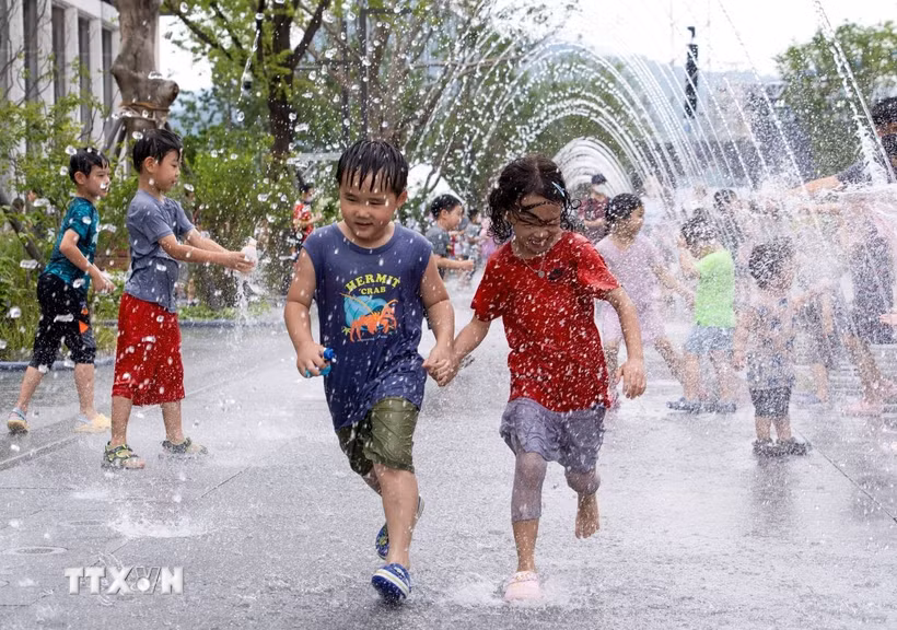 Các em nhỏ chơi đùa bên đài phun nước để tránh nóng tại Seoul, Hàn Quốc. (Ảnh: THX/TTXVN)