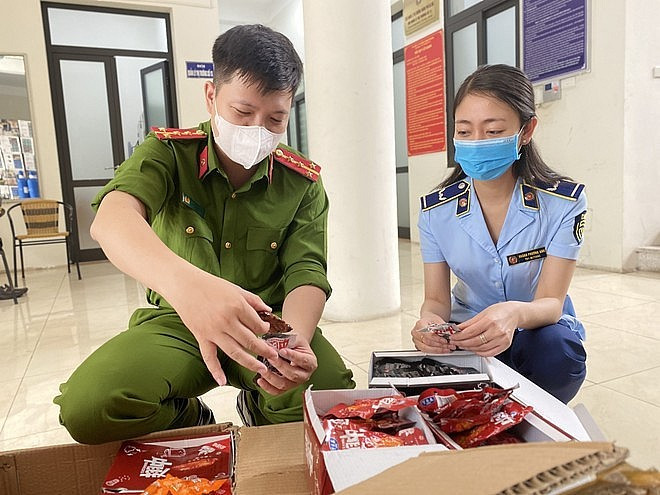 Lực lượng Công an và Quản lý thị trường kiểm tra hàng hóa vi phạm. (Ảnh: PV/Vietnam+) Thu hơn 6.000 sản phẩm xúc xích và cánh gà ăn liền không rõ nguồn gốc ảnh 1
