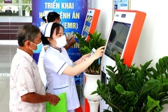 Nhân viên y tế hướng dẫn người dân đăng ký khám bệnh qua hệ thống kios tự động tại Bệnh viện Đa khoa Trà Vinh, tỉnh Vĩnh Long. (Ảnh: TTXVN)