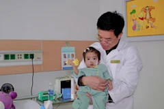 Phó giáo sư Lê Văn Thành thăm bé Di sau hơn một tháng phẫu thuật. (Ảnh: PV/Vietnam+)