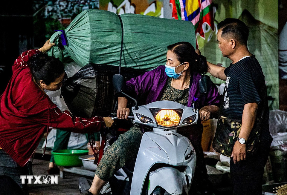 Từ tờ mờ sáng, người dân đã chở theo nguyên liệu và những chồng nón đã hoàn thiện trên xe máy, tấp nập đổ về khu vực sân đình để họp chợ. (Ảnh: Vân Chi/TTXVN phát)