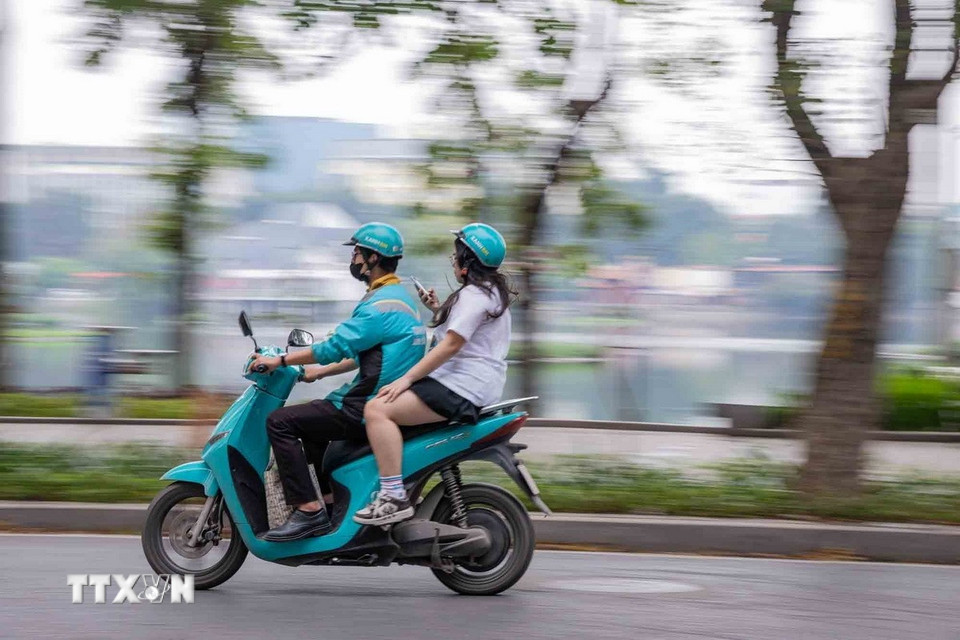 Tài xế xe công nghệ sử dụng xe máy điện chở khách di chuyển trên tuyến đường Nguyễn Du (Hà Nội). (Ảnh: Phạm Tuấn Anh/TTXVN)