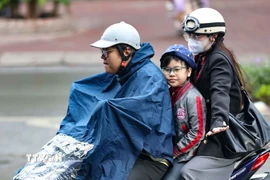 Một gia đình ra đường trong chiếc áo mưa khi trời có mưa phùn. (Ảnh: Thanh Tùng/TTXVN)