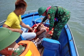 Chiến sỹ Đồn Biên phòng Ngọc Vừng hỗ trợ đưa ngư dân gặp nạn sang tàu khác an toàn. (Ảnh: TTXVN phát)