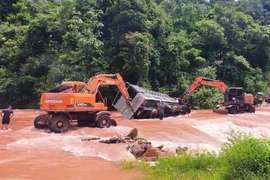 Xe tải bị lật nghiêng khi đi qua điểm bị ngập, dòng chảy mạnh. Lực lượng chức năng, người dân địa phương phải chèn bánh và dùng xe cẩu nỗ lực kéo xe tải ra khỏi vị trí nguy hiểm. (Ảnh: TTXVN phát)