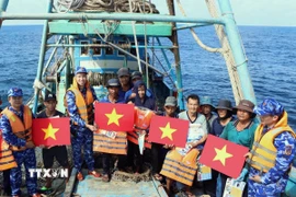 Lực lượng chức năng tặng cờ Tổ quốc, áo phao cho ngư dân trên biển. (Ảnh: TTXVN phát)