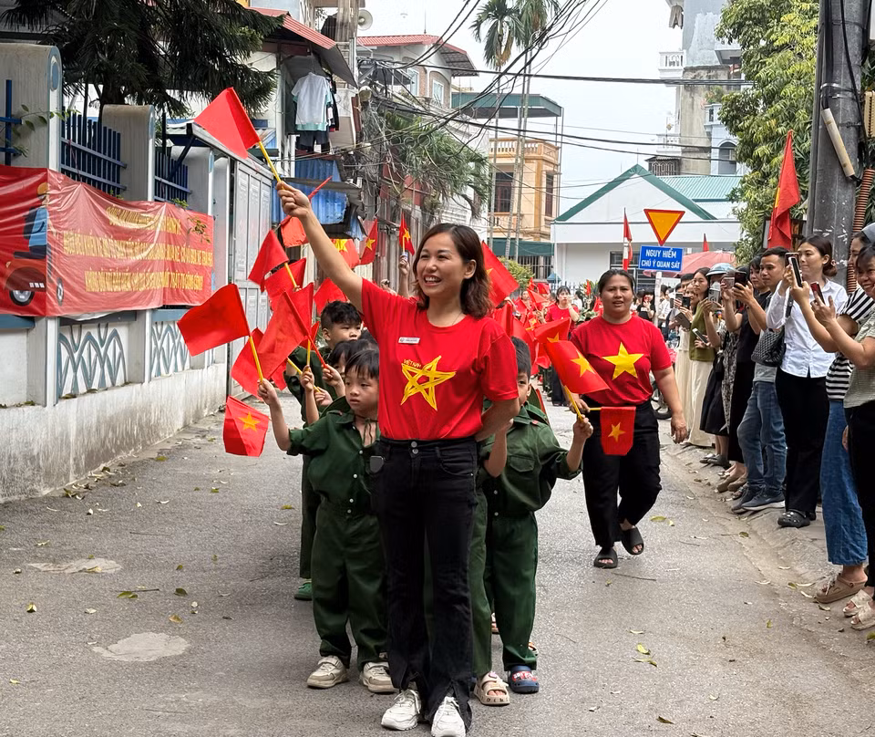 Giáo viên, học sinh cầm cờ đỏ sao vàng tái hiện hình ảnh diễu binh, diễu hành. (Ảnh: PV/Vietnam+)