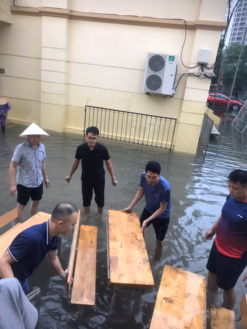 Để học sinh, phụ huynh không phải lội nước, các thầy cô giáo Trường Tiểu học Nam Trung Yên đã kê bàn ghế làm cầu giúp phụ huynh đón con, học sinh không bị dầm nước. (Ảnh: PHCC)
