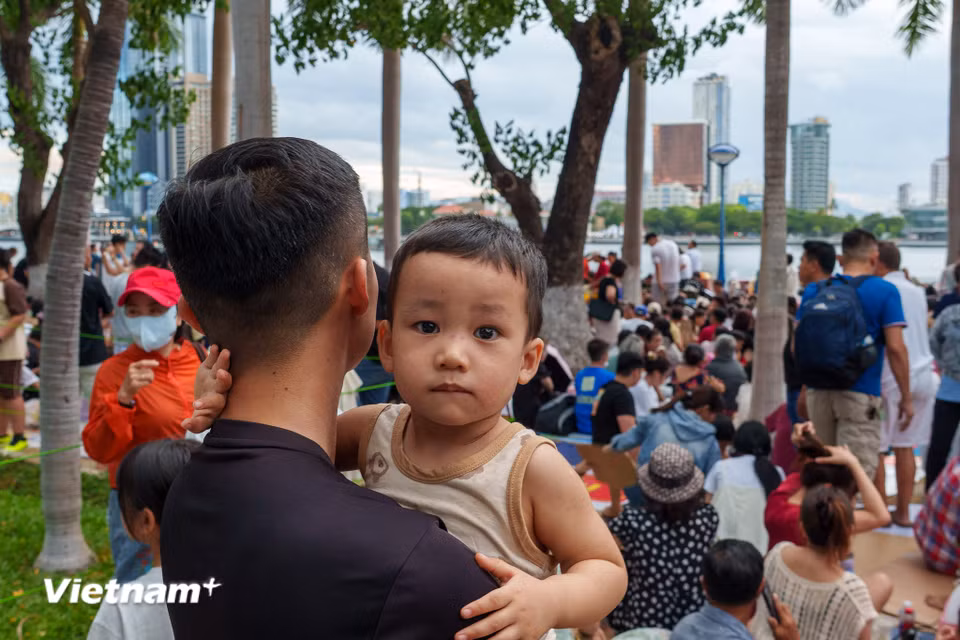 Một em nhỏ được người thân bế trên tay, ngơ ngác giữa biển người đông đúc chờ xem pháo hoa. (Ảnh: Thanh Phong/Vietnam+)