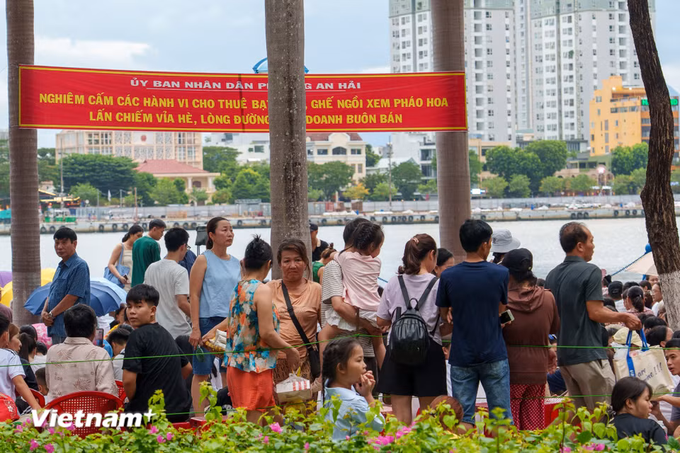 Người dân trật tự ngồi xem pháo hoa phía sau hàng rào và băng rôn cấm lấn chiếm vỉa hè kinh doanh. (Ảnh: Thanh Phong/Vietnam+)