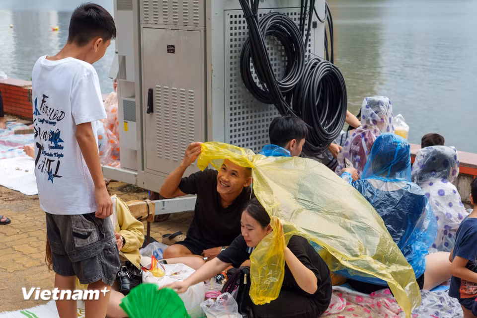 Những chiếc áo mưa, ô dù được tận dụng tối đa để che chắn trong lúc mỏi mòn chờ đợi pháo hoa rực sáng. (Ảnh: Thanh Phong/Vietnam+)
