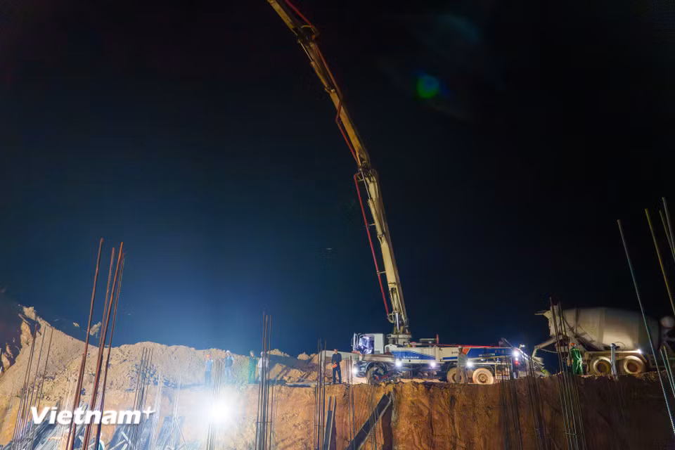 Xe bơm bê tông vươn cần cẩu khổng lồ, phối hợp nhịp nhàng cùng xe bồn trộn để truyền vật liệu xuống vị trí thi công đài móng sâu bên dưới. (Ảnh: Thanh Phong/Vietnam+)
